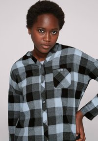 Camicia a maniche lunghe a quadri in nero, grigio e azzurro chiaro. Chiusura anteriore con bottoni, colletto e taschino singolo sul petto. Tessuto morbido con motivo a scacchi.