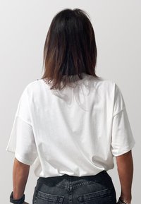 T-shirt bianco oversize con maniche corte e collo rotondo, realizzata in tessuto morbido e leggero. Indossato con jeans in denim scuro.