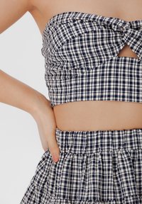 Jūros jėgos ir grietinėlės spalvos checkered trumpas viršus su surištu priekiu ir išpjovos detale, derinamas su atitinkama sluoksniuota sijonu su elastinga juosta.