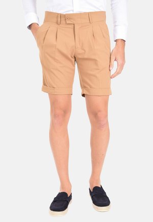 Pantaloni corti beige realizzati in tessuto leggero, con due pieghe frontali, risvolti e chiusura con bottone, abbinati a scarpe scure.