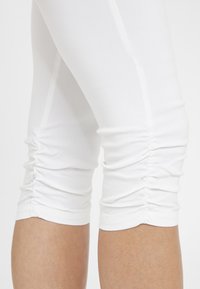 Witte capri leggings met geplooide details aan de onderrand, gemaakt van een soepele, rekbare stof voor comfort en bewegingsgemak.