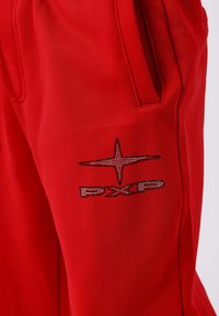 Pantalones rojos con un bolsillo lateral y un diseño brillante en forma de estrella sobre las letras "DXP" cerca del bolsillo.