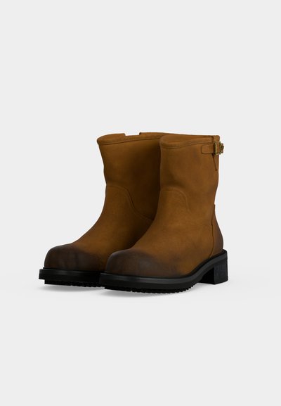Paire de bottes mi-mollet en daim marron avec semelles en caoutchouc noir et petits talons carrés, avec une petite sangle à boucle près du haut.