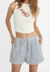 Cropped white tank top with a red lobster graphic, paired with blue and white striped shorts featuring an elastic waistband and drawstring.