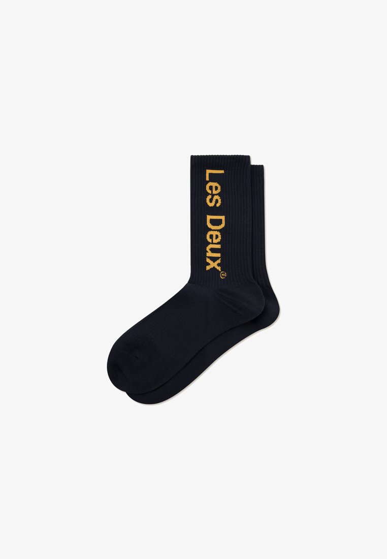 Meias pretas com nervuras que apresentam o logo "Les Deux" em texto dourado na lateral. Textura suave, comprimento alto até o tornozelo e design simples.
