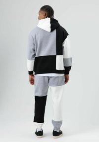 Color-blocked tracksuit featuring a gray, black, and white design. The hoodie has an oversized fit, with ribbed cuffs and a drawstring hood.
