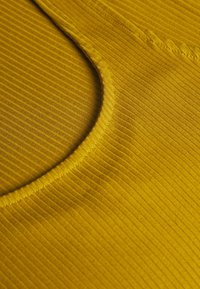 Tissu à côtes jaunes avec un col rond, texture lisse et couture visible le long du bord. Vue en gros plan.