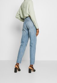 Jeans de tiro alto de color azul claro con un diseño de pierna recta, que cuentan con bolsillos traseros y un ajuste relajado, combinados con una camiseta de manga larga verde.