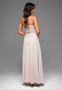 Lungo vestito rosa pallido con schiena lacciata, spalline regolabili e una silhouette fluida. Tessuto liscio, design minimalista.