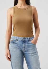 Ljusbrun ribbad ärmlös topp med rund halsringning, tillsammans med ljusblå denimjeans med knappstängning och fickor.