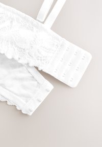 Bretelle de soutien-gorge en dentelle blanche avec bretelle réglable et fermeture à agrafe sur fond clair.