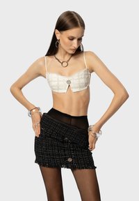 Witte gehaakte crop top met een knoopdetail, gecombineerd met een zwarte textuur mini rok met een rafelige zoom en twee knopen. Zwarte kousenpanty gedragen.