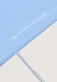 Lichtblauwe paraplu met een zilverkleurig handvat, met "TOM TAILOR" merknaam in witte letters nabij de rand.