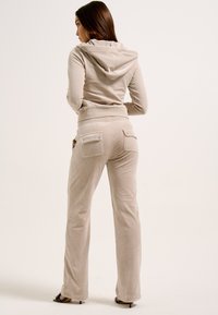 Beige velour tracksuit featuring a cropped hoodie and flared pants with back pockets. Smooth texture and subtle sheen; relaxed fit.