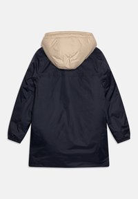 Giacca impermeabile blu navy con cappuccio beige, maniche lunghe, polsini elastici e vestibilità ampia. Texture liscia, dettagli minimi, vista posteriore.