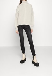 Jasnoszary gruby sweter z golfem w grubym splocie, zestawiony z czarnymi obcisłymi dżinsami i czarnymi butami na platformie o fakturowanej powierzchni.