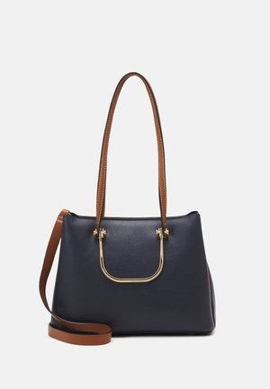 Bolso de mano de cuero azul marino con correas marrones para el hombro y un adorno de hardware dorado en forma de U. Diseño estructurado con textura suave.