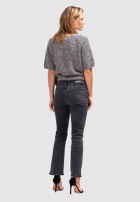 Haut en tricot gris à manches courtes et jeans skinny gris foncé, avec une taille haute, un ajustement cintré et des sandales à talons noires. Design simple.
