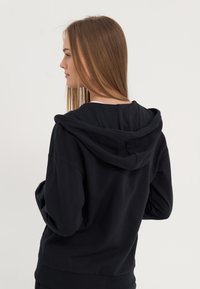 Sweat à capuche noir, en coton, coupe décontractée, avec des poignets et un ourlet côtelés, et une légère texture visible. La vue de dos montre une capuche couturée.