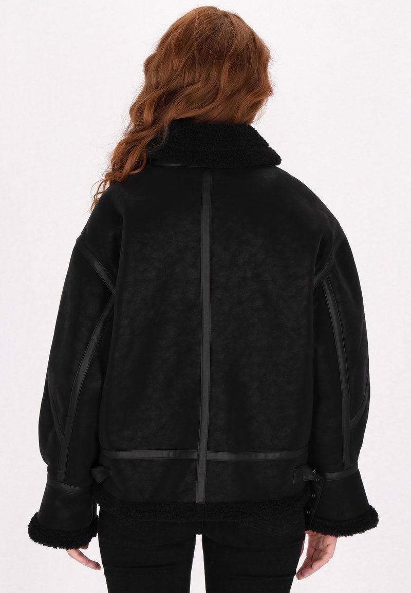 Schwarze Jacke mit strukturiertem Finish, Schaffellkragen und kontrastierenden schwarzen Akzenten. Hat eine lockere Passform und weite Ärmel.