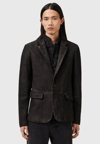Blazer de cuero negro con un corte entallado, que presenta un cuello con muescas, dos bolsillos frontales y cierres de botón. Textura suave y diseño casual.