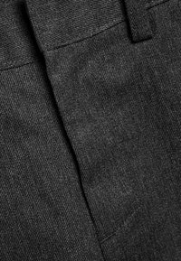 Tessuto grigio scuro con una trama texturizzata mette in risalto i dettagli di cucitura e un design pulito, enfatizzando un aspetto sartoriale contemporaneo.