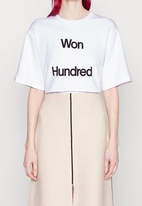Camiseta blanca de gran tamaño con texto negro "Won" y "Hundred". Combinada con una falda beige que presenta una apertura frontal y ribete negro.