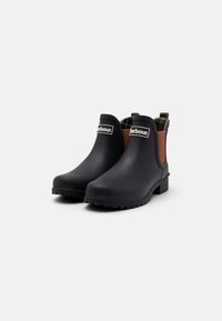Botas de borracha pretas até ao tornozelo com painéis laterais elásticos castanhos, uma superfície texturizada e uma sola robusta. Rótulo da marca na parte da frente.
