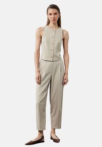Top sin mangas color beige con botones en la parte delantera, combinado con pantalones de tiro alto y corte recto en un tono a juego; la modelo lleva zapatos planos marrones.
