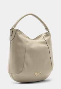 Borsa in pelle beige con forma arrotondata, dotata di un manico chiodato e di un logo dorato sul davanti. Texture liscia e design minimalista.