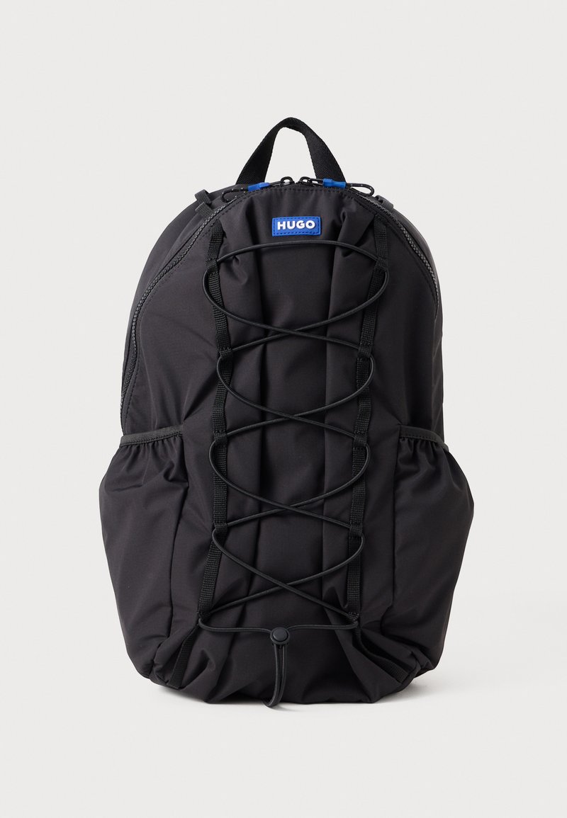 Mochila preta feita de tecido durável, com um design de corda bungee na frente, bolsos laterais e uma alça superior para transporte.