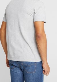 Šedé bavlněné tričko s krátkými rukávy, kulatým výstřihem a bez ozdob na zadní straně. Spárované s modrými džíny z denimu s prošíváním na zadních kapsách.