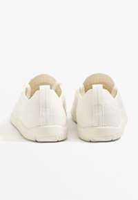 White mesh slip-on shoes with a smooth textured finish, featuring a pull tab on the back and a flexible rubber sole.
