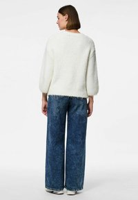 Vit, texturerad tröja med trekvartslånga ärmar, matchad med högmidjade blå vida jeans med fransade fållar.