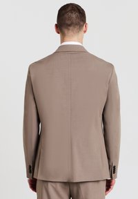 Beige Sakkoblazer mit glatter Textur, einzelner Rückenschlitz und schwarzen Knöpfen an den Ärmeln. Maßgeschneiderte Passform und klassisches Reversdesign.