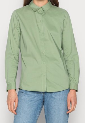 Light green long-sleeve shirt with a collared neck and button closure, made of smooth fabric. Paired with light blue denim jeans.