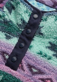 Tissu en polaire doux dans des tons de vert, violet et bleu avec des boutons-pression bleu marine embossés du mot "Superdry" sur un bord texturé.