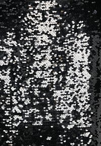 Tissu à sequins noirs et argentés avec des sequins circulaires réfléchissant la lumière, disposés en un motif créant des formes contrastées et une texture.