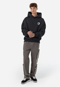Black hooded sweatshirt with a front logo, gray cargo pants featuring zippered pockets, and black sneakers with white laces.
