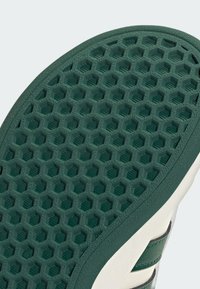Close-up of a green shoe sole with a hexagonal pattern and part of a white and green shoe upper visible.