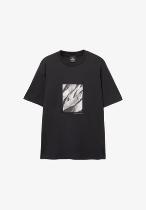 Černé tričko s krátkým rukávem z bavlny, s obdélníkovým grafickým potiskem v odstínech šedi zobrazujícím texturované vlny na přední straně.
