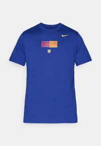 Blå bomuld t-shirt med et stribet flaggrafik i rød og gul, en lille logo nedenfor, og en kontrasterende gul Nike swoosh på skulderen.