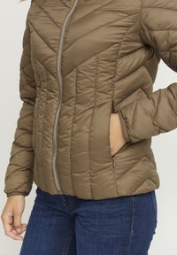 Padded jacket v olivovozelenej farbe so zipsovým zapínaním, s chevronovým šitím a bočnými vreckami, vyrobená z lesklého, ľahkého materiálu.