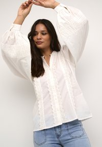 Weiße Baumwollbluse mit großen Puffärmeln, verziert mit Spitzenbesatz und Knöpfen auf der Vorderseite, kombiniert mit hellblauen Denim-Jeans.