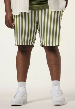 Underkrop af person iført grønne og hvide lodrette stribede shorts, hvide sokker og hvide sneakers på lys baggrund.