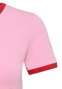 Gros plan d'une chemise rose à manches courtes avec un col rouge et des poignets rouges sur un fond blanc uni.