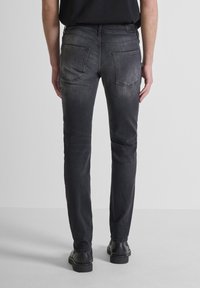 Uske slim-fit crne traperice s izblijedjelim izgledom, standardnog struka s pet petlji za remen, dva stražnja džepa i glatkom teksturom.