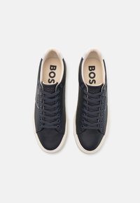 Tumedad sneakerid tekstureeritud nahast pealmise, lame paelte, beeži sisekatte ja kontrastse valge kummitaldiga. Logo külgedel.