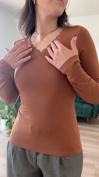 Hosszú ujjú, testhez álló felső meleg barna színben, fodros V-nyakkivágással. Puha bordázott textúra, szürke nadrággal párosítva.