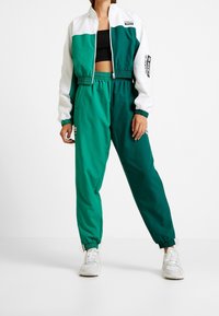 Tealfärgad och vit kort jacka med dragkedja, elastiska ärmar, tillsammans med tealfärgade byxor med elastisk midja. Båda har en sportig design och fickor.